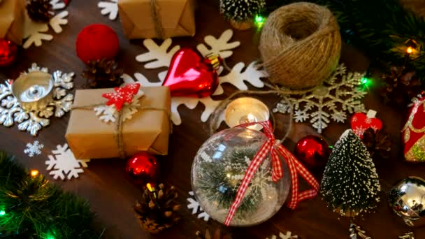 Kerstmis en Nieuwjaar achtergrond met cadeautjes, verlichting, kaarsen en andere decoraties. Gift in Kraft papier met red fir tree. — Stockvideo