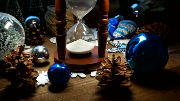 Kerstmis en Nieuwjaar achtergrond met cadeautjes, linten, ballen en verschillende groene versieringen op houten achtergrond. Houten zandloper maatregelen tijd tot vakantie. — Stockvideo