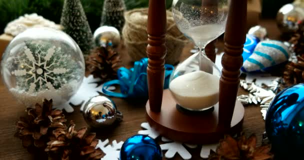 Vánoce a nový rok na pozadí s dárky, stuhy, plesy a různé zelené dekorace na dřevěné pozadí. Dřevěné přesýpací hodiny opatření čas do dovolené. — Stock video