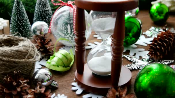 Natale e Capodanno sfondo con regali, nastri, palle e diverse decorazioni verdi su sfondo di legno. Clessidra di legno misura il tempo fino alla vacanza . — Video Stock