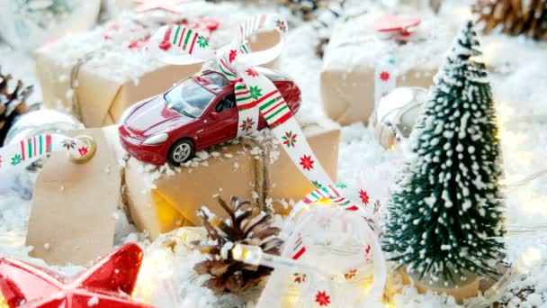 Weihnachten und Neujahr Hintergrund mit Spielzeugauto Geschenk mit Schleife. Kugeln, Tannenzapfen und verschiedene Dekorationen auf Schnee. — Stockvideo