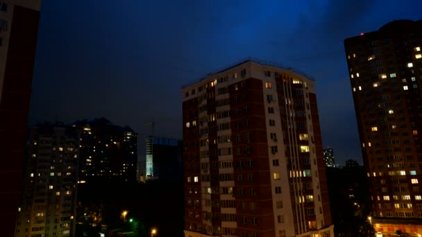 Timelapse do céu noturno sobre edifícios de apartamentos. Nuvens flutuam no céu, a luz brilha pelas janelas das casas . — Vídeo de Stock