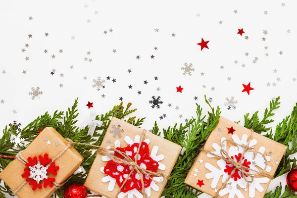 Χριστούγεννα και Πρωτοχρονιά φόντο με υποκατάστημα τούγιες, διακοσμητικά και δώρα τυλιγμένα σε χαρτί βιοτεχνίας με νιφάδες χιονιού. Επίπεδη lay, κορυφαία προβολή. — Φωτογραφία Αρχείου