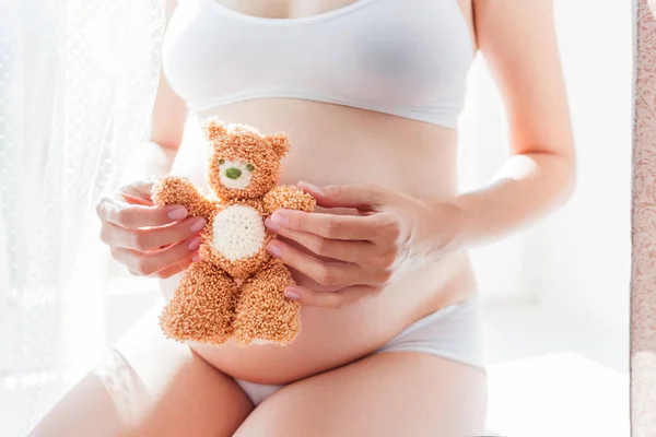 Mujer embarazada en ropa interior blanca con oso de juguete. Mujer joven esperando un bebé . —  Fotos de Stock