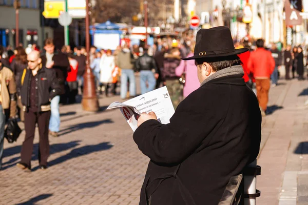 MOSCÚ, RUSIA - 25 de marzo de 2007. Hombre leyendo papel, gente caminando por la calle Arbat. Día de primavera cálido y soleado . — Foto de Stock