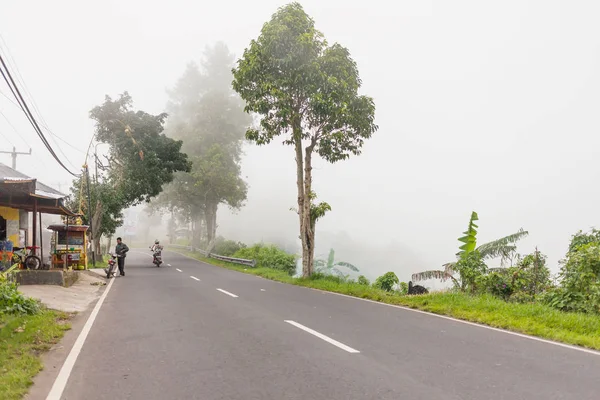 金塔马尼，印度尼西亚-2013 年 1 月 26 日。在路上，恶劣天气对驾驶摩托车的大雾。透过朦胧的常绿丛林森林的路。冬季多雨的季节。印度尼西亚. — 图库照片