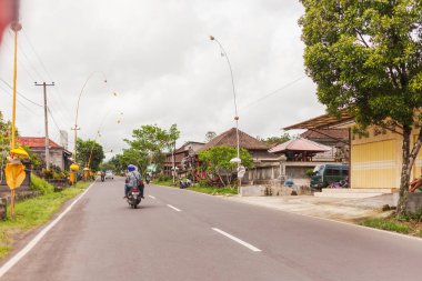 Ubud, Endonezya - 26 Ocak 2013. Dini dekorasyon yakınındaki evleri sokak. Bulutlu gün trafikte yol.
