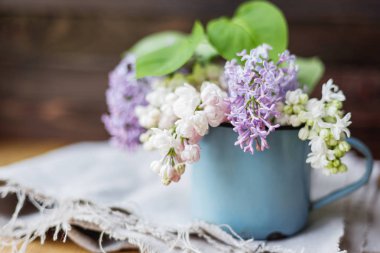 Leylak (Syringa) eski paslı kupa çiçeklenir. Ahşap masa üzerinde rustik Kupası beyaz ve mor çiçekli bahar arka plan.