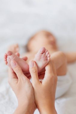Anne, yeni doğan bebeğin çıplak ayak tutar. Kadın eli küçük ayaklarda. Rahat sabah evde.