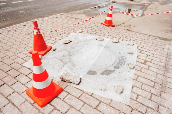 Los conos rojos de plástico advierten a los peatones sobre la reparación de la acera y la escotilla de alcantarillado. Moscú, Rusia . — Foto de Stock