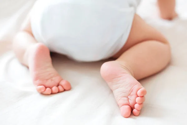 Barnets fötter. Lilla barnet bär vita bodysuit och blöja. Mysig morgon läggdags hemma. — Stockfoto