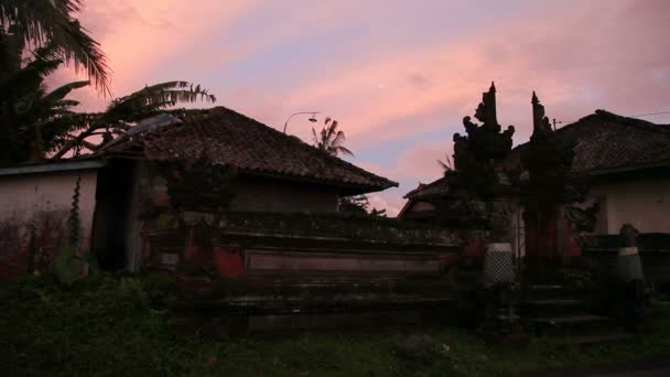 Silhuetter av husen med traditionella balinesiska dekorationer i solnedgången. Bali, Indonesien. — Stockvideo