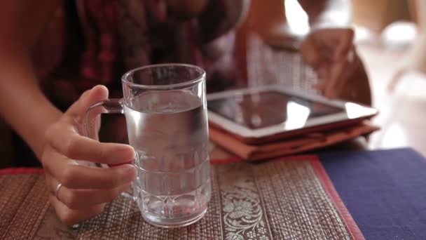 Ženu srazil hřebíky v zapocené sklenici studené vody a posouvání obrazovky tabletu. Kambodža. — Stock video