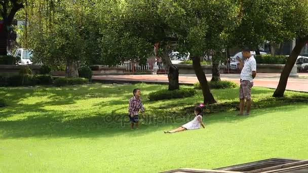 BANGKOK, TAILANDIA - 20 de octubre de 2012. Hombre tailandés grabar vídeo en el teléfono inteligente cómo sus hijos jugando. Ocio familiar en el parque . — Vídeo de stock