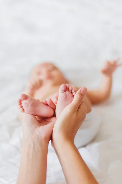 La madre sostiene los pies desnudos del bebé recién nacido. Pequeños pies en la mano de una mujer. Acogedora mañana en casa . — Foto de Stock