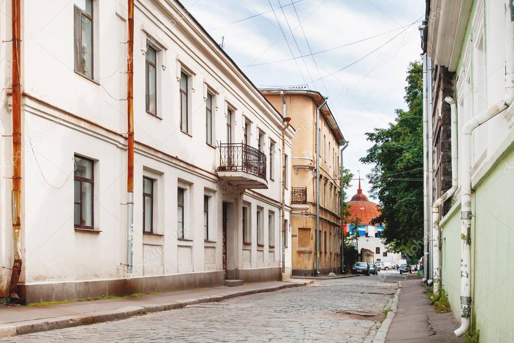 Old houses in Vyborg, Russia. Buildings with old fashioned windows and downpipes. Round Tower in the end of street.