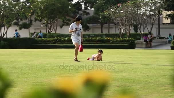Bangkok, Tajlandia - Październik 22, 2012. Miejscową kobietę nagrywa film na smartfon jako jej córka, grając z trawy. Wypoczynek dla rodzin z dziećmi w parku. — Wideo stockowe