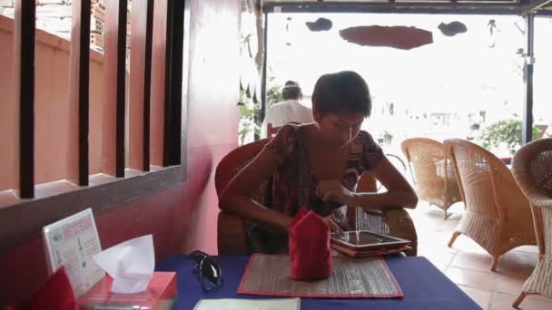 Kobieta siedzi w kawiarni i przesuwanie ekranu tabletu. Kambodża. — Wideo stockowe