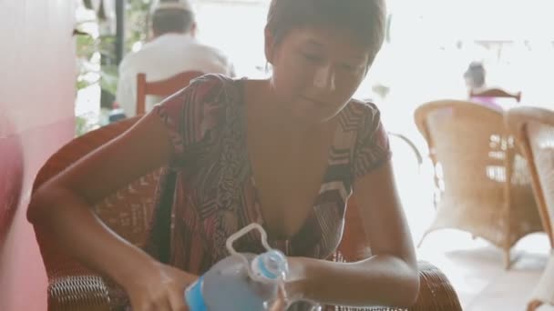 Mulher sentada no café e enchendo um copo com água de uma garrafa de plástico. Camboja . — Vídeo de Stock
