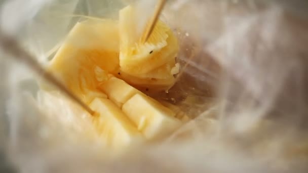 Plastic zak met plakjes verse ananas. Vrouw steekt een stukje ananas op een houten stokje. Traditionele Aziatische methode van het eten van fruit. Thailand. — Stockvideo