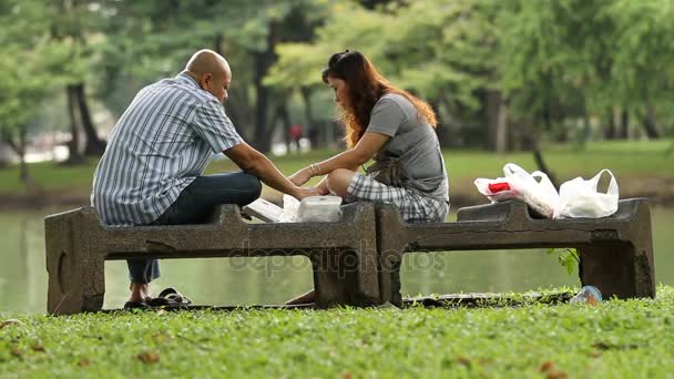 БАНГКОК, ТАИЛАНД - 24 октября 2012 года. Пара ест еду на вынос на скамейке в парке. Обед на открытом воздухе в парке Лумпини . — стоковое видео