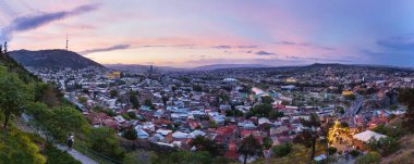 Tbilisi, Georgia ülkeden Narikala kale başkenti günbatımı panorama görünümünü. Ünlü simge - Metekhi kilise, kutsal Trinity Katedrali (Sameba), Cumhurbaşkanlığı yönetim, aydınlatma ile barış Köprüsü. 