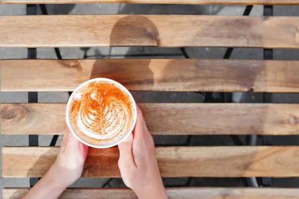 Frau hält eine Papptasse mit Kaffee. Coffee to go. Leckeres Heißgetränk auf Holztisch an sonnigen Tagen. Mahlzeit im Freien. flache Lage, Draufsicht. — Stockfoto