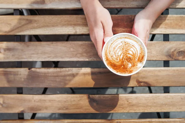 Mulher segurando uma xícara de papel com café. Café para levar. Bebida quente saborosa na mesa de madeira no dia ensolarado. Refeição ao ar livre. Deitado plano, vista superior . — Fotografia de Stock