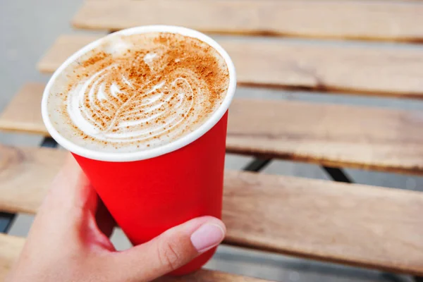 Mulher segurando uma xícara de papel vermelho com café. Café para levar. Bebida quente saborosa na mesa de madeira no dia ensolarado. Refeição ao ar livre . — Fotografia de Stock