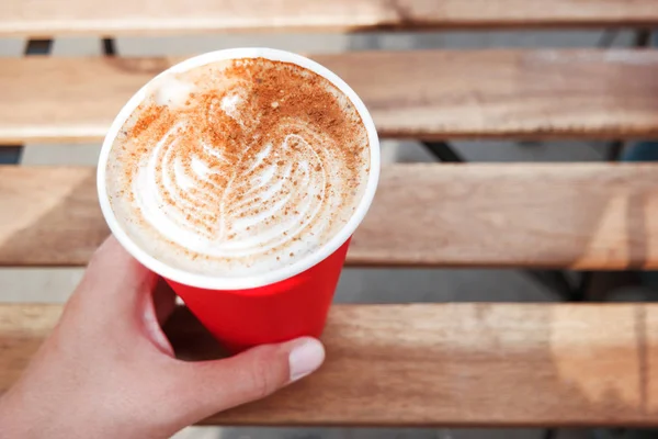 Vrouw met een rood papier beker met koffie. Koffie te gaan. Lekkere warme drank op houten tafel in zonnige dag. Openlucht maaltijd. — Stockfoto