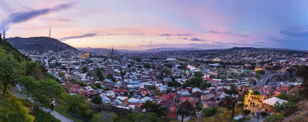 Vista panorámica al atardecer de Tiflis, capital del país de Georgia, desde la fortaleza de Narikala. Monumentos famosos - Iglesia de Metekhi, Catedral de la Santísima Trinidad (Sameba), Administración Presidencial, Puente de la Paz con iluminación . — Foto de Stock