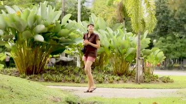 Turist Lumpini Park toplayan fotoğraflar. Kadın farklı bitki ve ağaçlar vuruyor. Bangkok, Tayland.