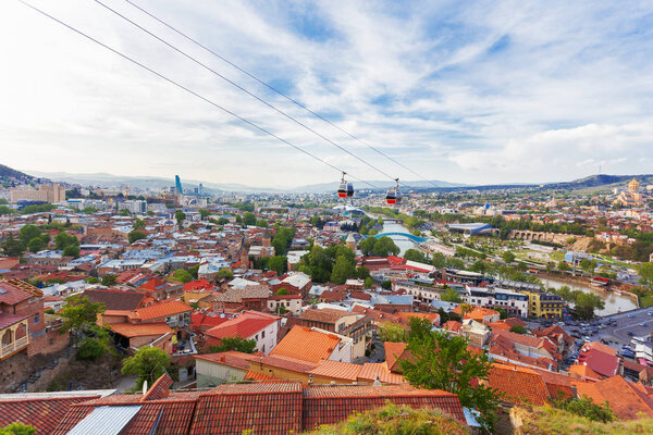 Panorama view of Tbilisi, capital of Georgia country. View from Narikala fortress. Cable road above tiled roofs.