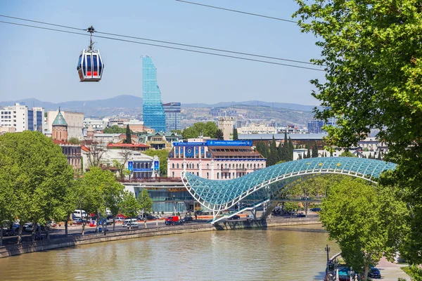 TBILISI, GEORGIA - 01 de mayo de 2017. Vista panorámica de los monumentos modernos Puente de la Paz y Biltmore Hotel Tbilisi. Cabina de carretera por cable deslizándose sobre la ciudad . — Foto de Stock