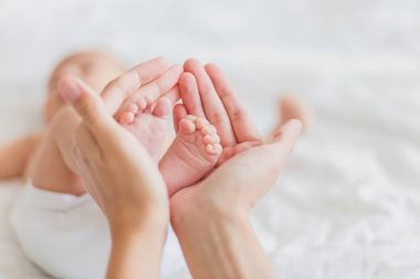 Anne, yeni doğan bebeğin çıplak ayak tutar. Kadın eli küçük ayaklarda. Rahat sabah evde.