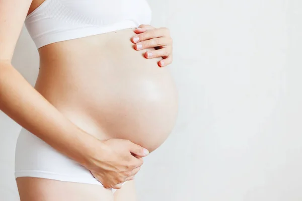 Beyaz iç çamaşırlı hamile kadın. Bebek bekleyen genç bir kadın..