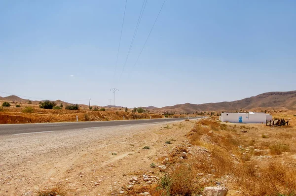 Camino en algún lugar de Túnez a través del desierto del Sahara. Paisaje de África con líneas eléctricas y carretera asfaltada . — Foto de Stock