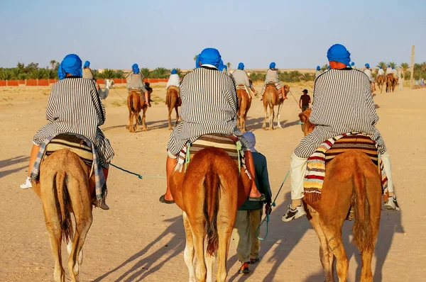 Turistas e beduínos em camelos encontram o pôr do sol no deserto do Saara. Tunísia — Fotografia de Stock