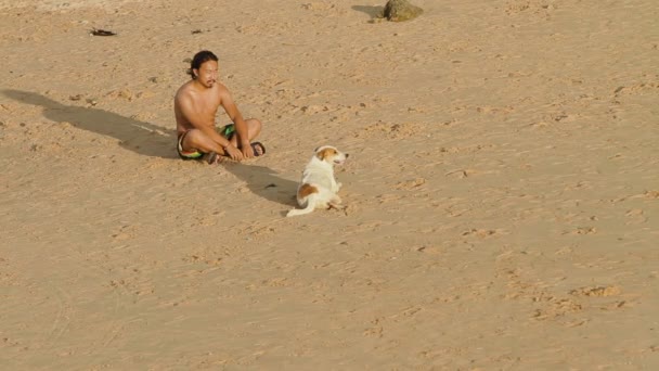 Phuket, Thailand - 18 November 2012. Lokale man met hond zittend op Nai Harn beach en vergadering zonsondergang. — Stockvideo