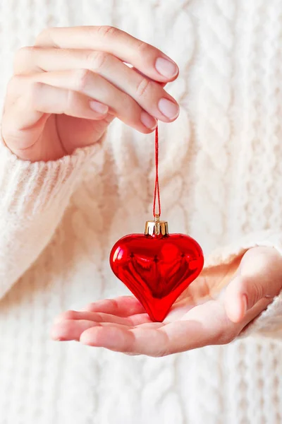 Femme en pull tricoté blanc tenant la décoration de Noël coeur rouge vif. Scintillant, brillant symbole de l'amour. Vacances Nouvel An ou Saint-Valentin fond . — Photo