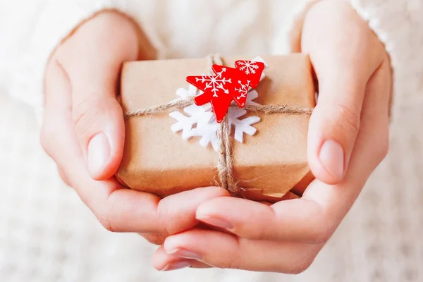 女士在针织毛衣举行新年礼物。礼品包装在工艺纸与白色毛毡雪花和红枞树。Diy 的方式来包装圣诞礼物. — 图库照片