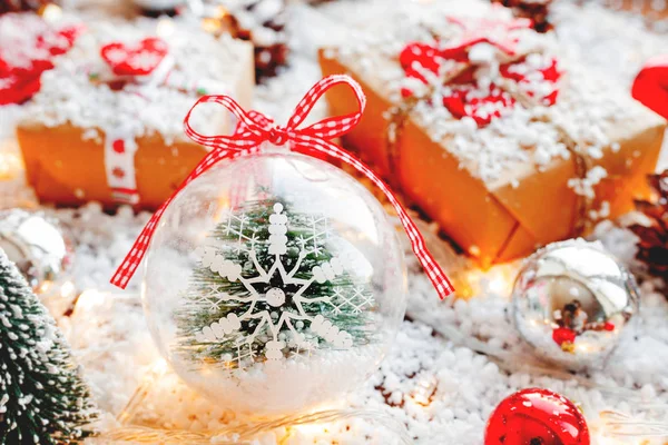 Karácsonyi és újévi háttér bemutatja, szalagok, labdák és más dekorációk a hó. Átlátszó labda, hópehely és fenyő fa belsejében. — Stock Fotó