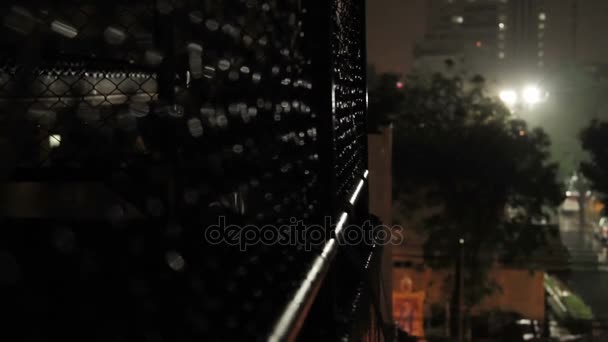 Nachtregen in Bangkok. Blick auf nasse Straße vom Balkon durch Rabitznetz. Thailand. — Stockvideo