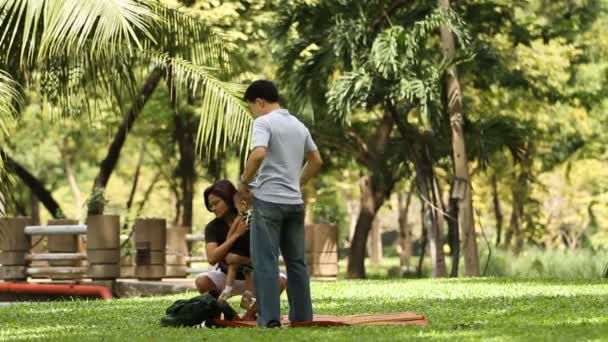 BANGKOK, TAILANDIA - 21 de octubre de 2012. La familia - los padres con el niño - se prepara para el picnic en la hierba. Los locales se relajan en el parque público . — Vídeo de stock