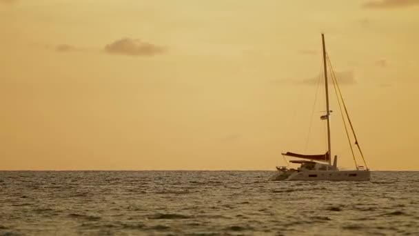 Tramonto sulla spiaggia di Naiharn. Lo yacht a vela ondeggia sulle onde. Nuvoloso su sfondo arancio tramonto . — Video Stock