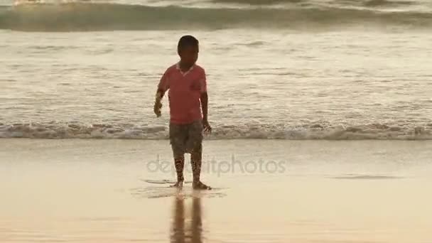 Phuket, Thailand - 18 November 2012. Kind spelen in de branding van de zee. De voeten van de kinderen in het water. Oranje zonsondergang weerspiegeling in golven van de zee. Phuket, Thailand. — Stockvideo