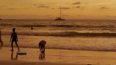 Phuket, Tayland - 18 Kasım 2012. Deniz sörf oynayan çocuk. Su ayaklarda çocuklar. Dalgalar deniz turuncu günbatımı yansıması. Phuket, Tayland.