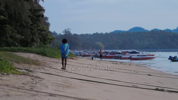 Phuket, Thailand - 20 November 2012. Zonsopgang op Rawai beach. Mensen en hond wandelen passeren rij van afgemeerd motorboten. — Stockvideo