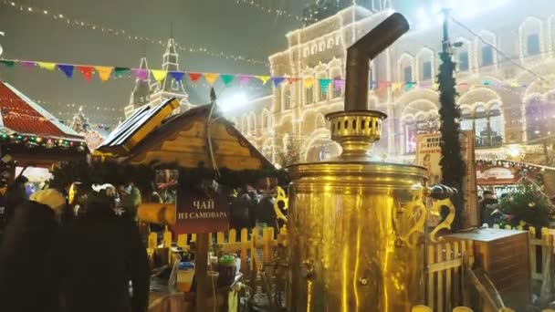 МОСКВА, РОССИЯ - 03 декабря 2017 года: Люди идут по Рождественской ярмарке на Красной площади. Уличное кафе с ярким золотым самоваром . — стоковое видео