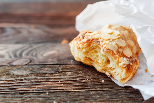 Tasty croissant in white paper bag on table. Rustic wooden background with sweet dessert.